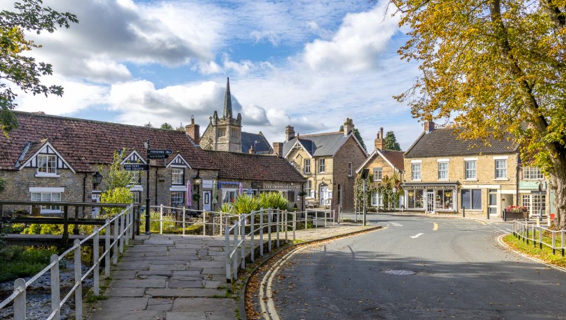 The centre of Thornton-le-Dale on a sunny autumn day, with stone cottages, the church spire and a fingerpost beside the beck