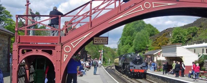 Steam locomotive arriving beneath the red iron footbridge at Goathland station on the North Yorkshire Moors Railway