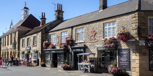 Stone shopfronts with hanging baskets around the market place at Helmsley in the North York Moors