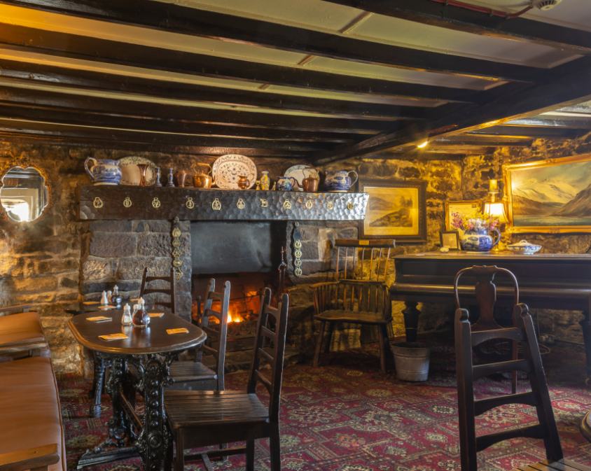 The panelled bar of a traditional North York Moors pub in winter, with a blazing log fire, dark beams and a piano in the corner