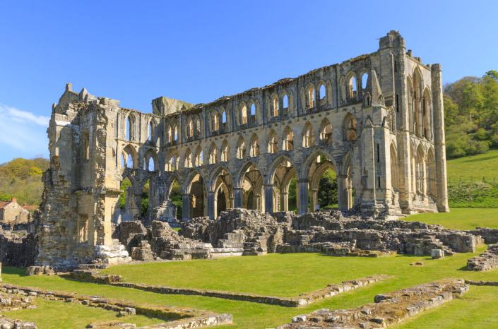 The tall stone arches and extensive ruins of Rievaulx Abbey in their green valley