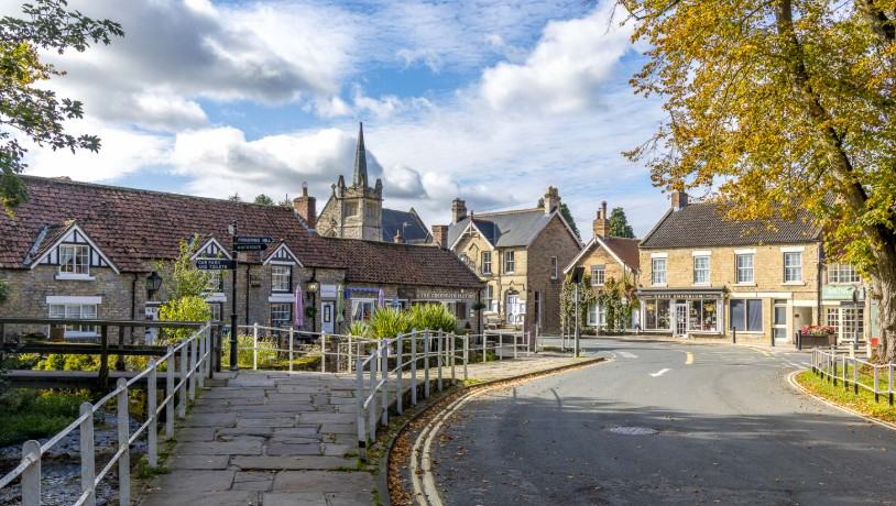 The centre of Thornton-le-Dale on a sunny autumn day, with stone cottages, the church spire and a fingerpost beside the beck
